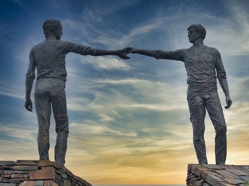 Two statues of men reaching out to each other.